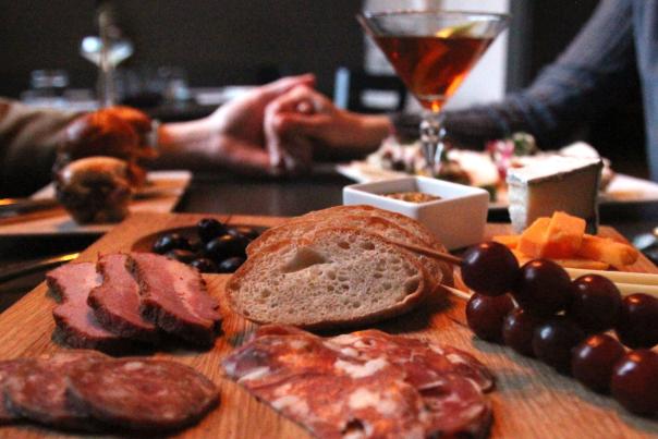 A couple holding hands at a table with a charcuterie board and martini
