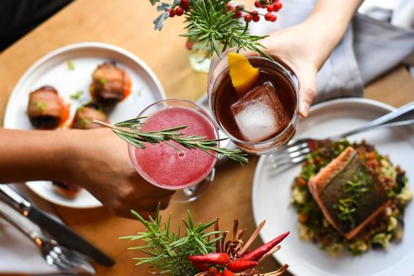 A birdseye view of two people clicking glasses over a table of food at Cardinal Spirits