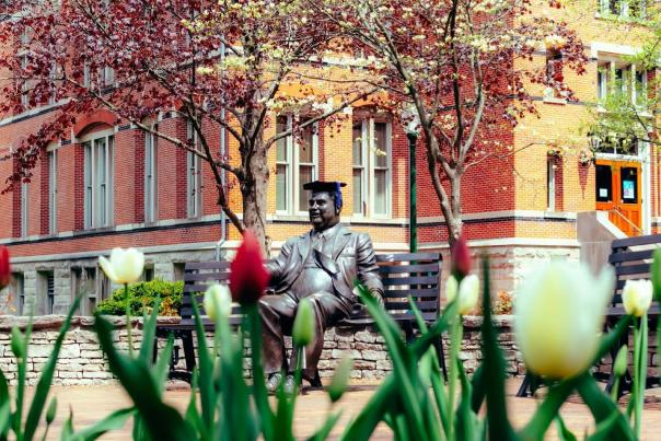 The Herman B Wells statue wearing a graduation cap on a spring day