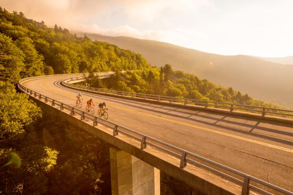 Three cyclists on the Blue Ridge Parkway's Linn Cove Viaduct, a bridge that weaves along the side of a mountain.