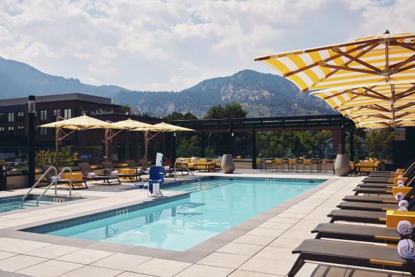 The rooftop pool with lounge chairs and yellow umbrellas with views of the Flatirons and foothills at Limelight Hotel, Boulder