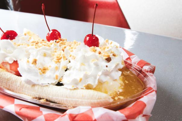 A classic banana split dessert from Billy Bob's Dairyland in Branson, Missouri, served in a plastic dish with red checkered paper and topped with whipped cream, crushed nuts, and three maraschino cherries.
