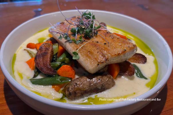 a piece of fish topped with greens and sitting on a bed of roasted vegetables in a bowl of grits from Fish Factory Restaurant and Bar in Southport, NC