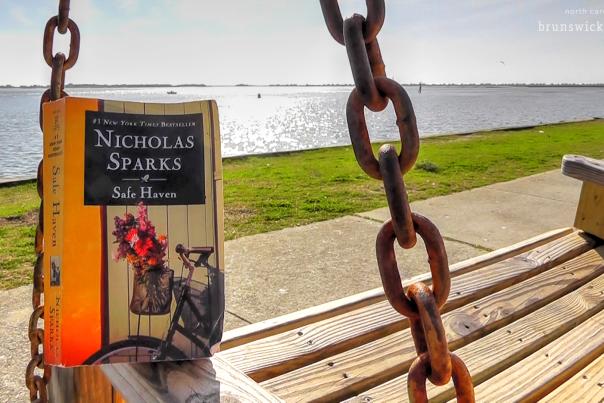 A paperback copy of "Safe Haven" by Nicholas Sparks sits on a swinging bench on the Southport, NC waterfront