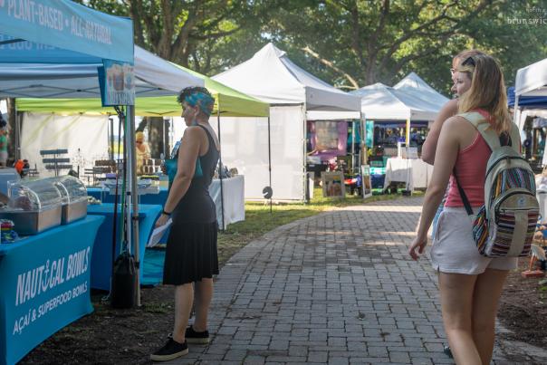 a woman ordering at a market stall as another woman walks past at the Sunset Beach Market in the Park