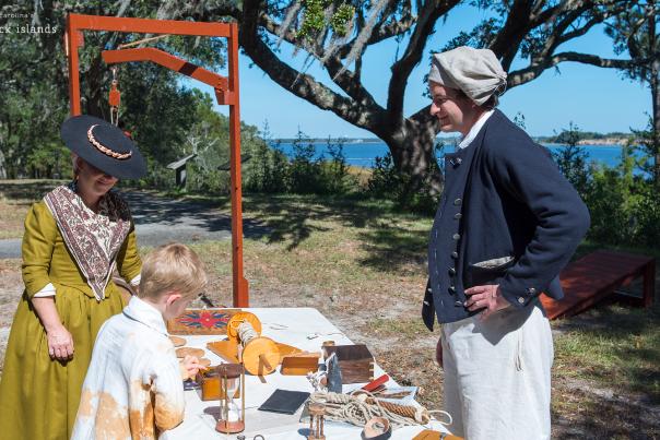 a man and woman in colonial costume show a kid items on a display table