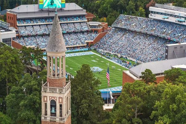 Aerial view of Kenan Stadium on the campus of the University of North Carolina with crowds in the seats and the Morehead Patterson Bell Tower in the foreground.