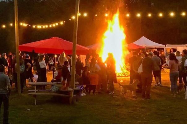 People sitting and standing around a big bonfire at Pluck Farm at the Renaissance Faire