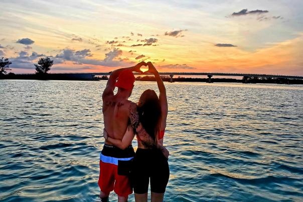 Couple standing in water at sunset, creating "heart hands"