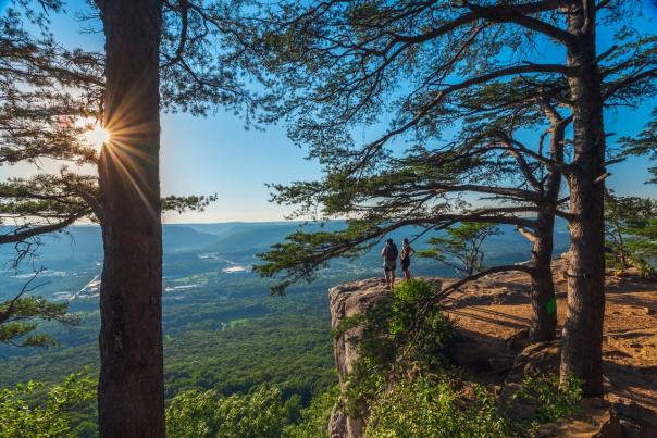 two people stand on side of cliff at sunset rock