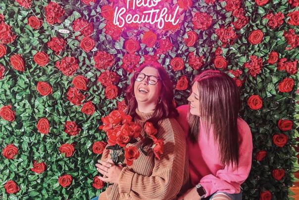 Women pose in front of wall of flowers at Selfie Museum