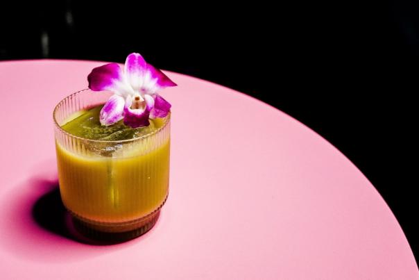 cocktail decorated with a flower sits on a pink table