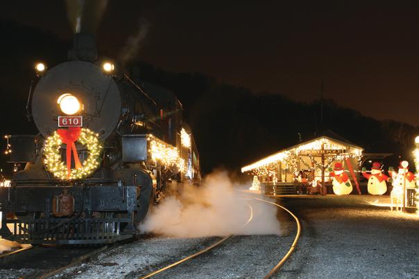 Train pulls away from station at night that's lit up with holiday lights