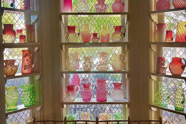 Multi-colored glass pictures are lined on shelves in a bay window at the Houston Museum of Decorative Arts