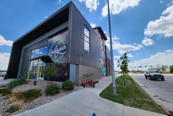 Modern architecture of The Railspur building in Cheyenne, featuring a large logo and vibrant mural on a sunny day.