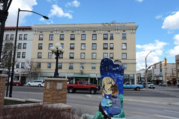 The Plains Hotel, a historic building in downtown Cheyenne, with a painted bison sculpture in the foreground and urban streetscape surrounding it.