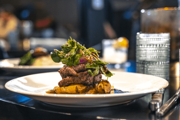 An elegant plated dish of steak and fresh greens, accompanied by a glass of whiskey, capturing the essence of a fine dining date night restaurant in Cheyenne.