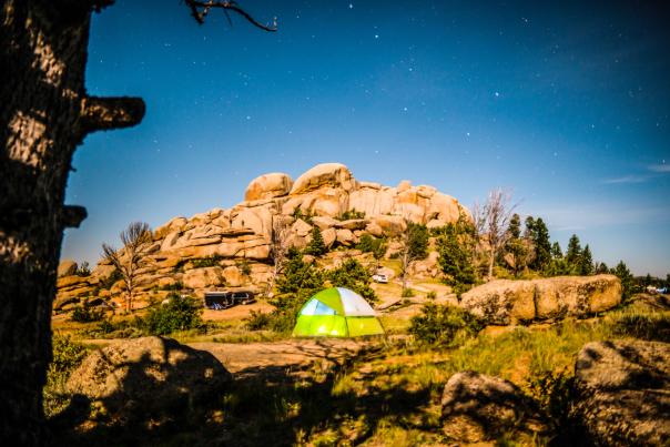 Green tent sits beneath a rock formation at Vedauwoo under a night sky full of stars.