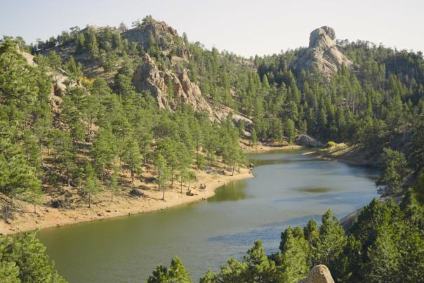 A peaceful lake surrounded by rocky hills and dense pine forests at Curt Gowdy State Park, one of the hidden gems near Cheyenne, ideal for hiking and nature lovers.