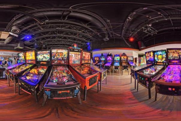 Panoramic view inside Flipper's arcade showcasing a vibrant array of colorful pinball machines under a curved ceiling with ambient lighting.