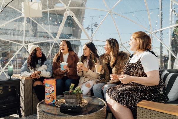 The image is of 5 women sitting inside an igloo that you can see out of during the day.