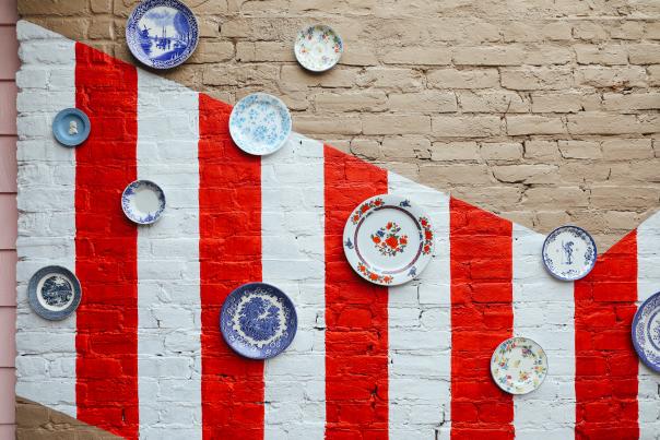 Image is of their outdoor patio plate wall in which they have antique plates of all shapes and sizes nailed to a brick wall.