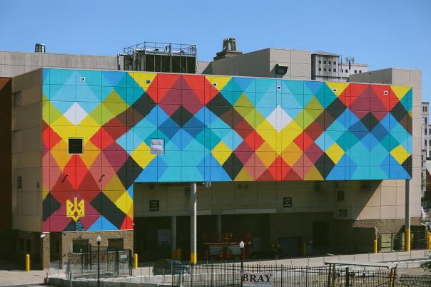 A large-scale mural on the side of a convention center features colorful criss-crossing line reminiscent of a weaving