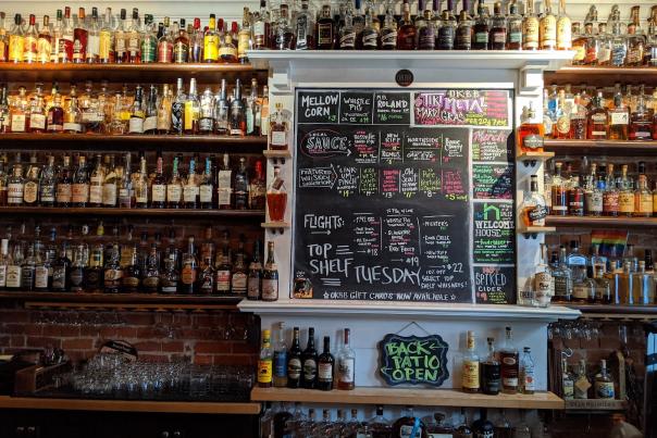 A wall covered in bottles of bourbon with a chalkboard menu at the center at OKBB