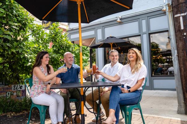 Four people enjoy cocktails at a patio table underneath a black umbrella at Rich's Proper in Covington