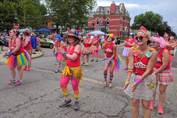 A group of people in red tops and brightly colored accessories dance at NKY Pride