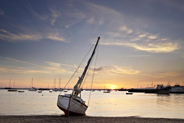 A boat sits on the shore of Mersea Island as the sun sets