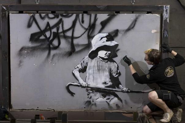 An artist works on a Banksy artwork.