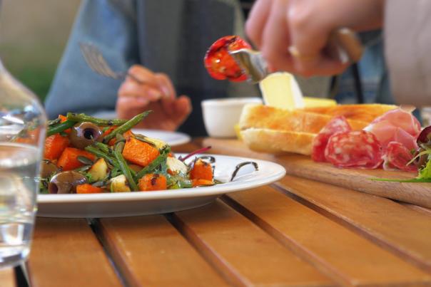 A diner enjoys a bright plate of food, including a salad and a charcuterie board.