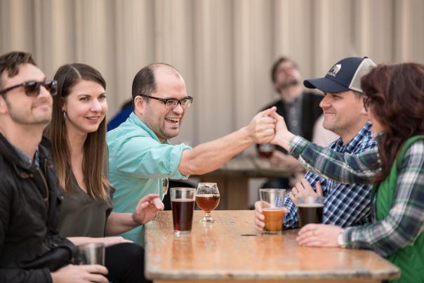 Friends handshaking over beers at an outdoor table at River Rat