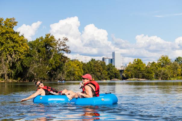 Two people in floats on the river with Columbia skyline in the background