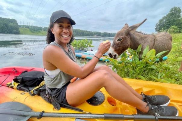 Smiling person in kayak with donkey nearby
