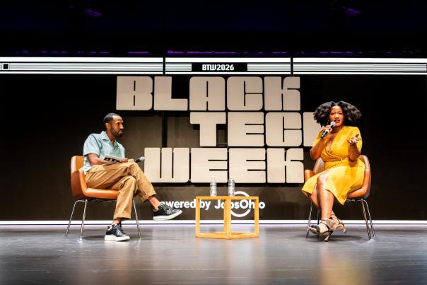 Two people sit in chairs on sage with "Black Tech Week" in the background