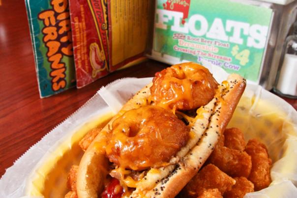 Loaded hot dog sitting on pile of tater tots on table at Dirty Frank's