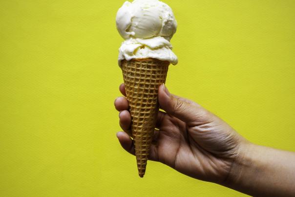 Outstretched arm holding ice cream cone in front of vibrant yellow background