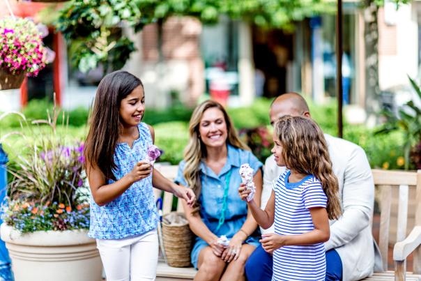 A mom and dad sit on a bench while happily watching their two girls hold ice cream cones