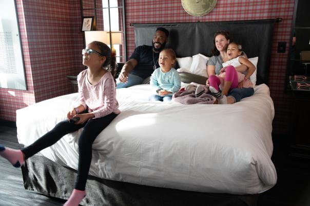 Parents and three kids sitting in bed in Graduate Columbus hotel room