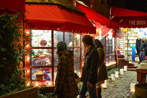 Three people bundled in winter apparel stare into an illuminated Book Loft from the outside