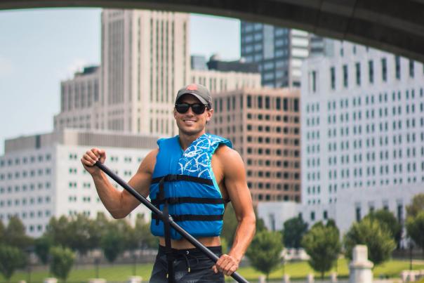 A man poses for a photo with the downtown skyline while paddleboarding on the Scioto River