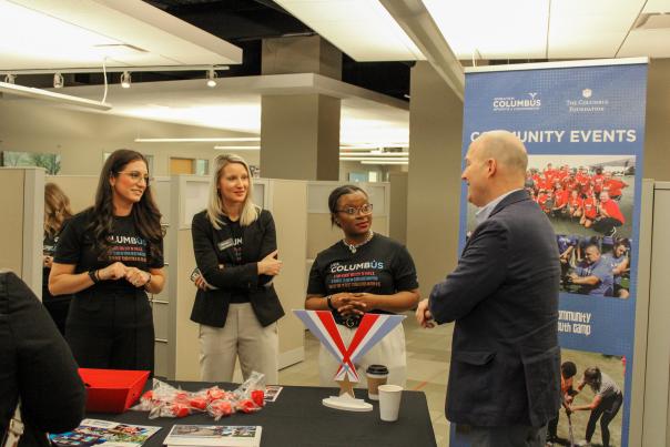 Three women stand listening intently to a man in a suit at the Experience Columbus Open House