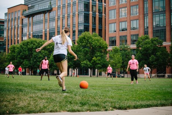 A woman about to kick a kickball into a field of other players
