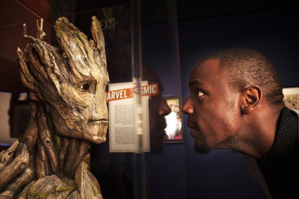 A man leans close to a Groot sculpture at COSI's Marvel exhibit