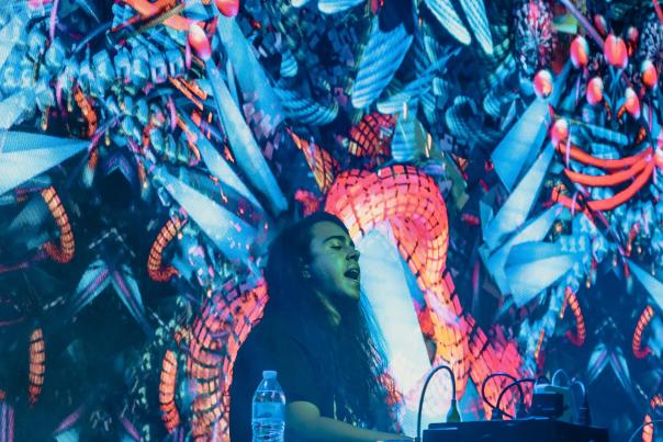 DJ Shatter performing at turntables in front of screen projections of colorful, psychedelic fractals