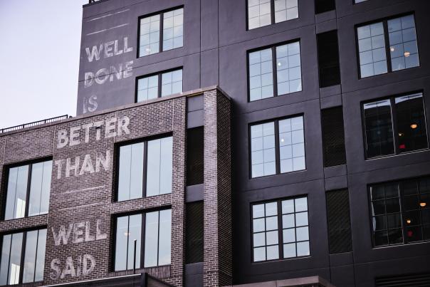 Mural on the outside of The Junto hotel saying "Well Done is Better Than Well Said"