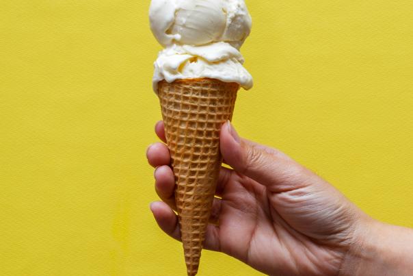Hand holding ice cream cone in front of vibrant yellow wall