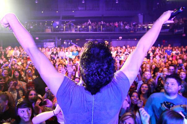 Musician with arms open facing large crowd of fans during concert